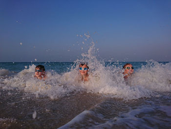 Boys swimming in sea against clear sky during sunset