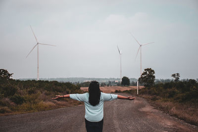 Rear view of woman with arms outstretched standing on road against sky