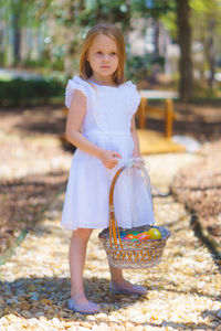 Cute girl wearing white dress holding easter eggs in basket at back yard