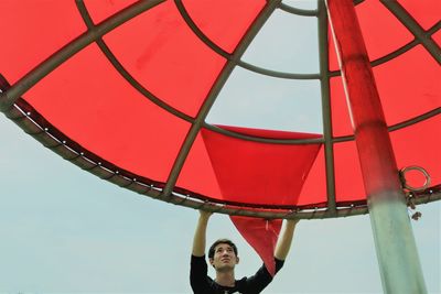 Low angle portrait of man with red umbrella against sky