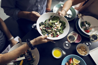 Cropped image of friends holding salad bowl at table
