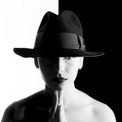 Portrait of young woman wearing hat with hands clasped against black background