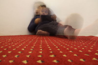 Portrait of woman sitting on bed against wall at home
