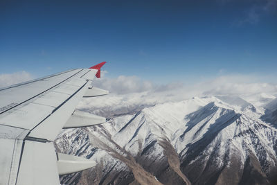 Airplane flying over snowcapped mountains against sky