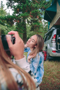 Woman photographing friend through camera in camp