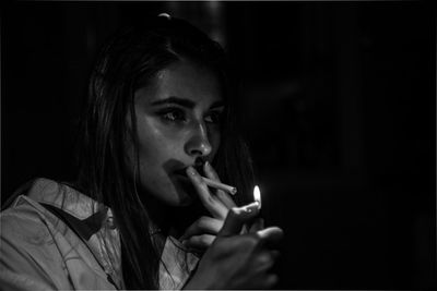 Close-up of woman igniting cigarette against black background