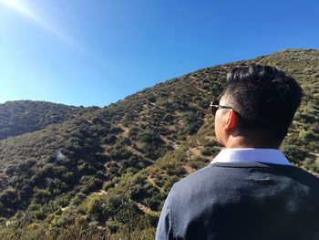 Rear view of man looking at mountain against blue sky