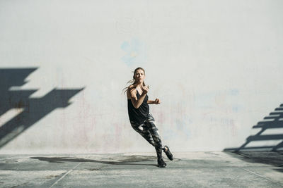 Determined female athlete exercising on sidewalk against white wall