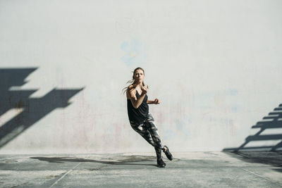 Full length of young woman jumping on wall