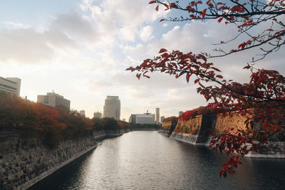 River amidst buildings against sky during autumn