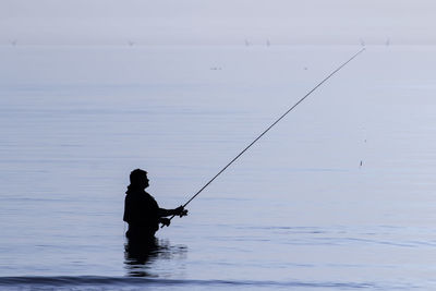 Silhouette man fishing in sea during sunset