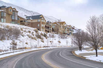 Snow covered road by buildings against sky