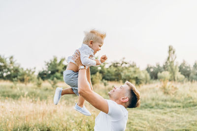 Side view of happy man playing with son on field against clear sky