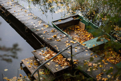 Old wooden fishing green boat stands at the pier on the lake in the village of autumn in cloudy