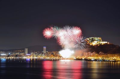 Firework display over illuminated city against sky at night