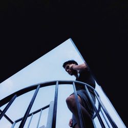 Low angle view of young man talking on mobile phone while standing on steps against sky