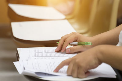 Midsection of woman writing on paper while sitting on table