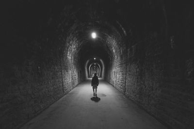 Rear view of man walking in illuminated tunnel