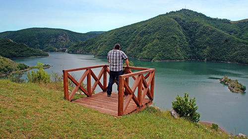 Rear view of man standing by lake against mountain
