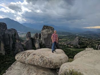 Full length of man standing on rock against cloudy sky