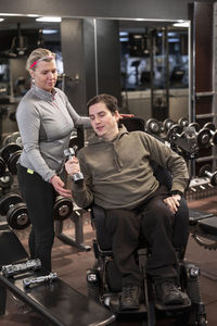 Man on wheelchair training in gym with personal trainer