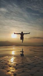 Silhouette man jumping on beach against sky during sunset
