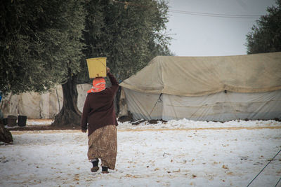 A refugee woman holds a bucket of water on her head during the snow in the camp.