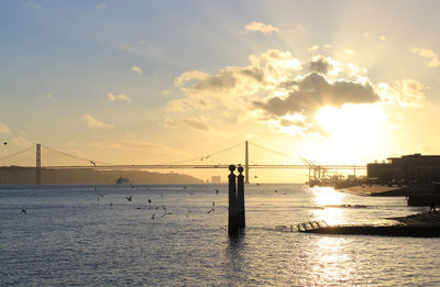 Suspension bridge over sea against sky during sunset