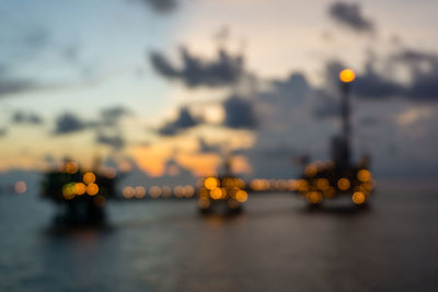 Illuminated city by sea against sky at sunset