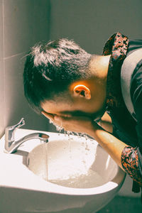Side view of man washing face in bathroom sink