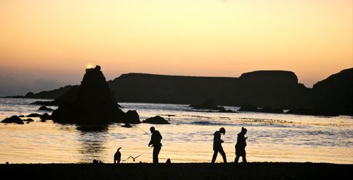Silhouette people on beach against sky during sunset