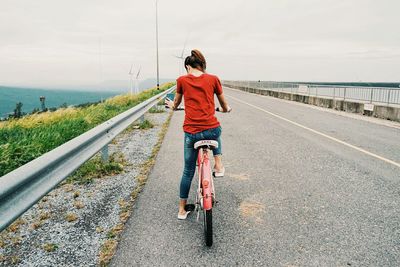 Rear view of woman riding bicycle on road against sea