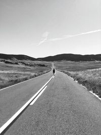 Road passing through field against sky