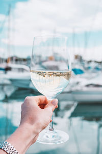 Woman hand with white wine, champagne glass on yachts, sailing boats background. nice, france.