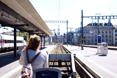 Rear view of woman standing at railroad station against sky