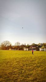 Side view of girl playing with ball while standing on grassy field against sky