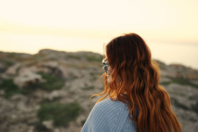 Rear view of woman standing at beach during sunset