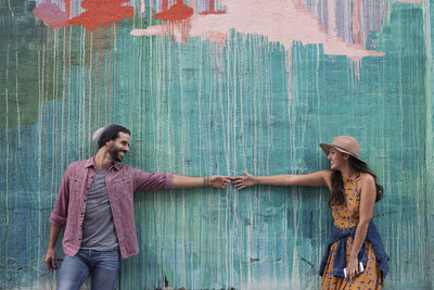 Happy young couple at a wall reaching for each other