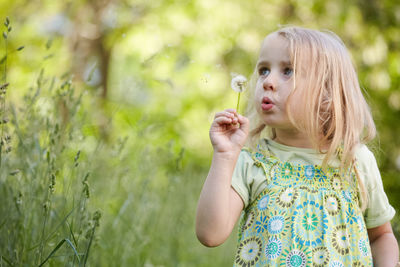 Cute girl blowing dandelion by plants