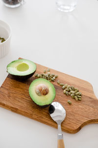 Still life sliced avocado with pumpkin seeds lies on a wooden board on a white table, top view.