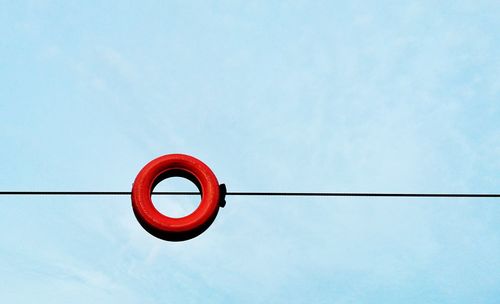 Low angle view of red tire on cable against blue sky