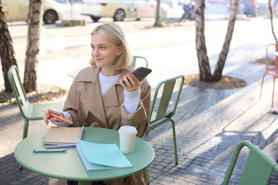 Young woman using mobile phone while sitting at cafe