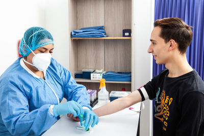 Young female nurse collecting a blood sample from a male patient in a clinic