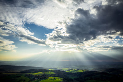 Sunbeams streaming through clouds over landscape