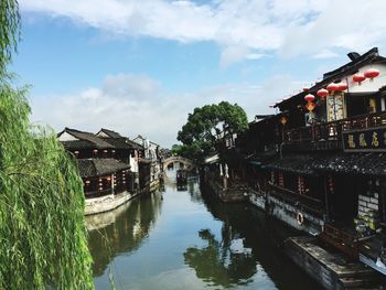 Canal amidst houses and trees against sky