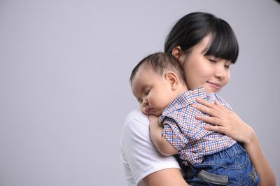 Woman carrying son against colored background