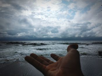 Close-up of hand on beach against sky