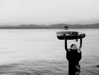 Close-up of coin-operated binoculars on sea against sky