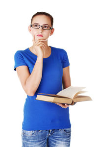 Portrait of beautiful young woman holding book while thinking against white background