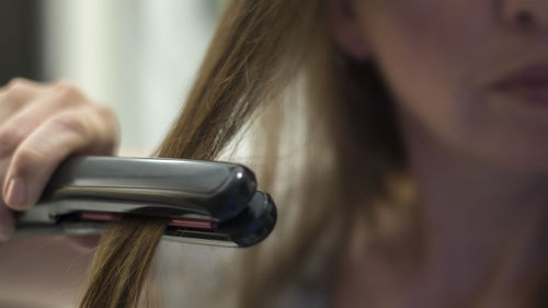 Close-up of woman straightening hair at home